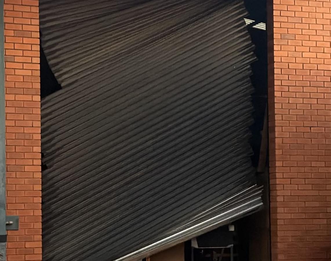 Black roller shutter door buckled out of its guides in a brick opening, awaiting emergency repair